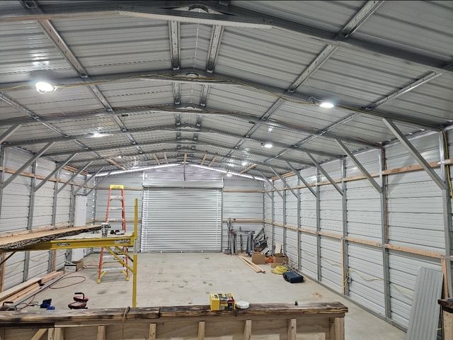Metal shop building interior with LED high-bay light fixtures and wiring run along the steel trusses